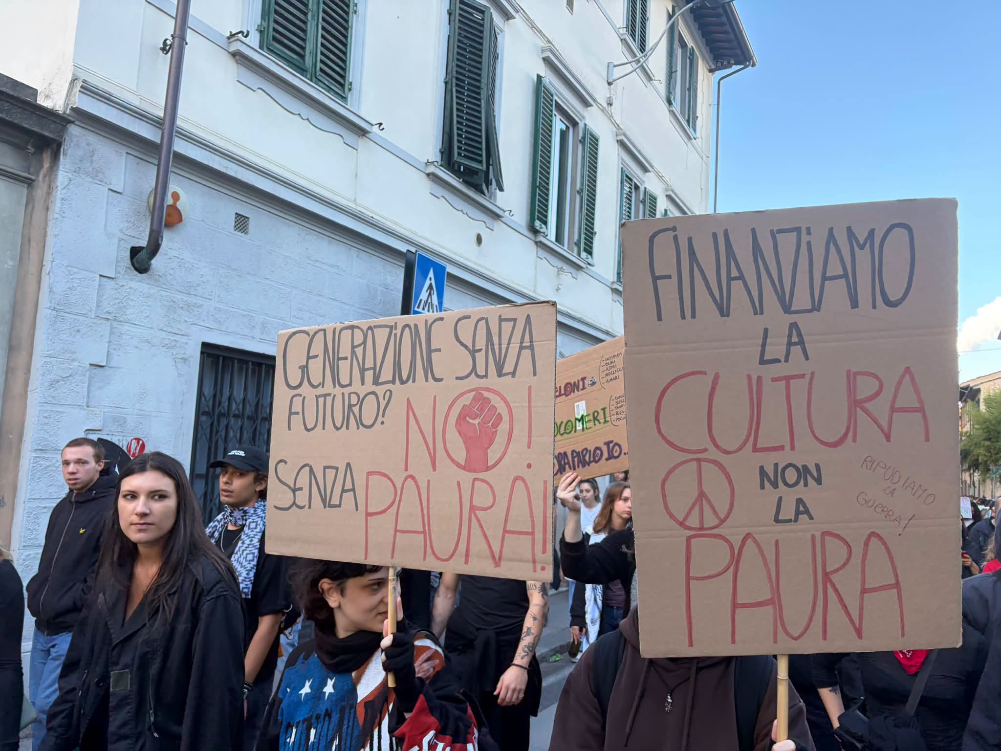 Due cartelli al corteo di Firenze del 24 ottobre 2026: «Generazione senza futuro? No! Senza paura» e «Finanziamo la cultura non la paura», con il simbolo della pace